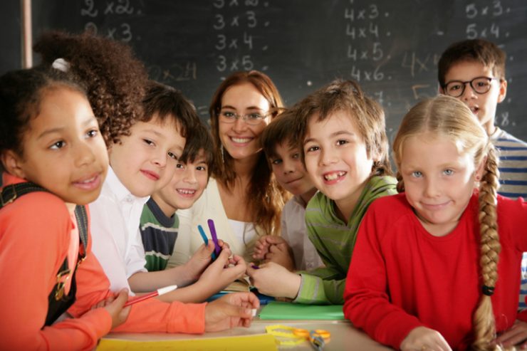 Schueler_innen mit Lehrerin laechelnd vor Tafel, Foto: iStock, Weekend Images Inc.