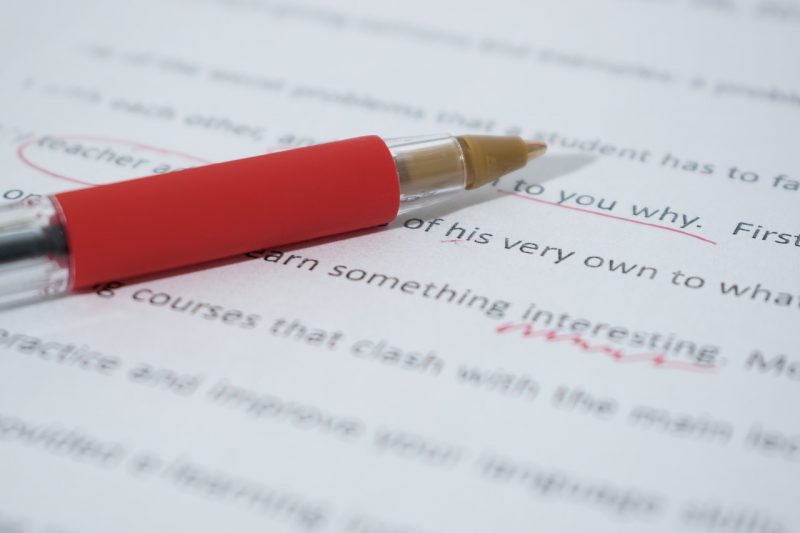 Nahaufnahme von gedrucktem Text, rote Anmerkungen. Roter Stift liegt auf dem Dokument