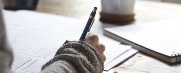 Unterarm liegt auf Schreibtisch mit Stift in der Hand, Hand schreibt etwas auf ein Papier