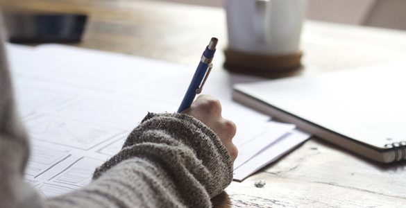 Unterarm liegt auf Schreibtisch mit Stift in der Hand, Hand schreibt etwas auf ein Papier