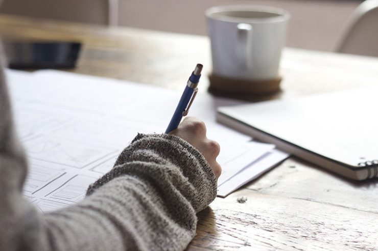 Unterarm liegt auf Schreibtisch mit Stift in der Hand, Hand schreibt etwas auf ein Papier