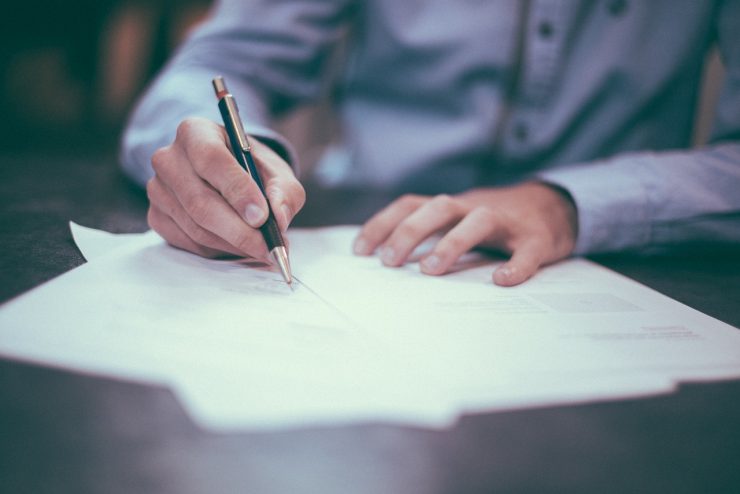 Person in Hemd mit Stift in der Hand, unterschreibt Blätter