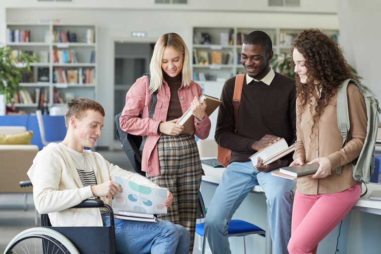 Porträt einer multiethnischen Gruppe von Studenten in der Hochschulbibliothek mit einem Jungen im Rollstuhl im Vordergrund, AdobeStock_Seventyfour