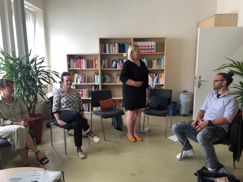 Drei in einem Stuhlkreis sitzende und eine stehende Person in einem Büro