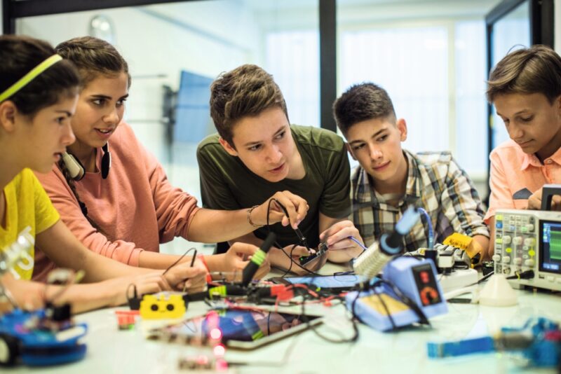 Teenage brother and sister, with other group of students, working on some robot project at electronic course. Working table full of different oscilloscopes and equpment needed for recording electrical circuits.